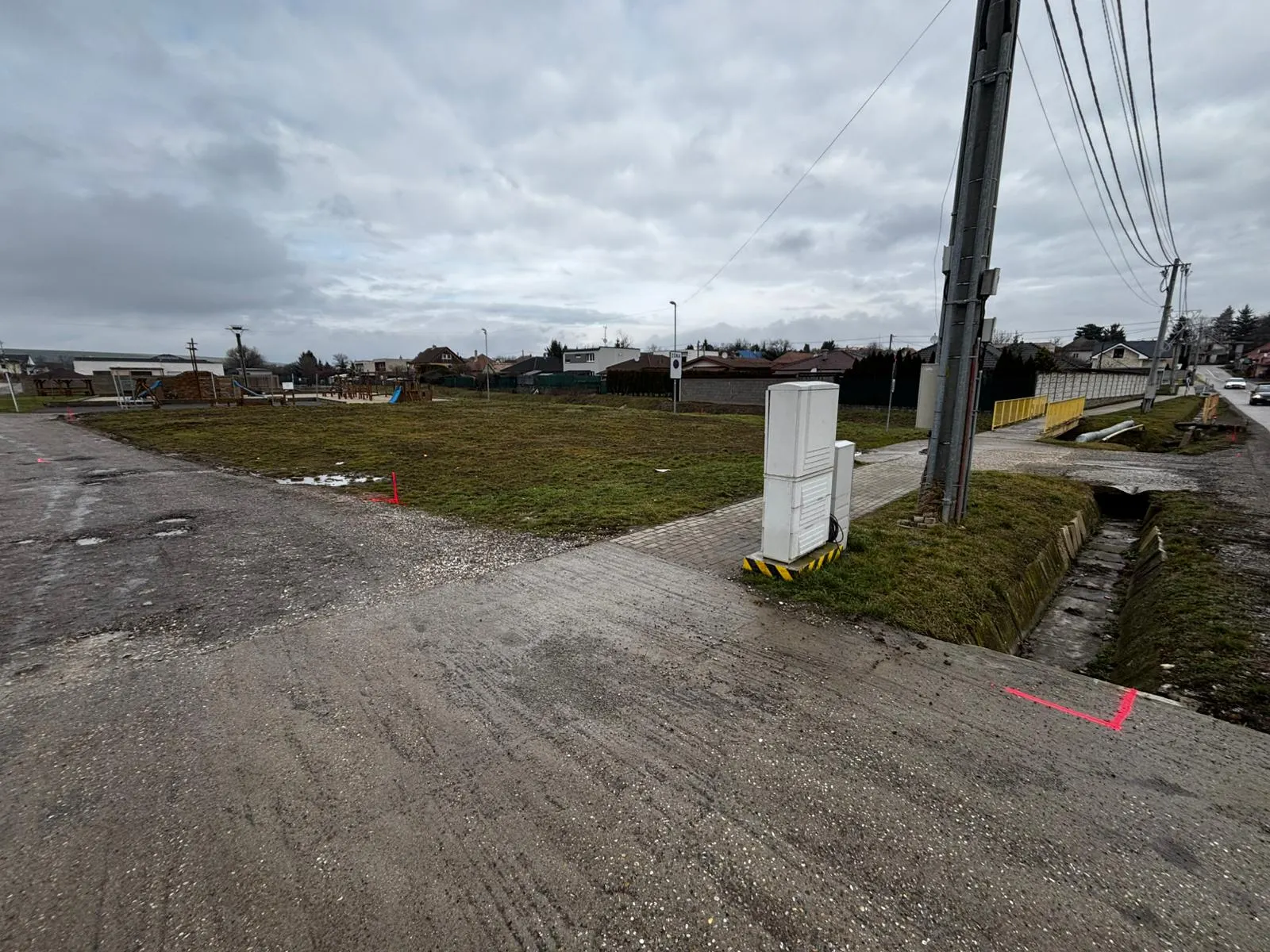 BEFORE — original state of the plot in the village centre (~1,200 m²). Red surveyor markers show the boundaries of the future building.