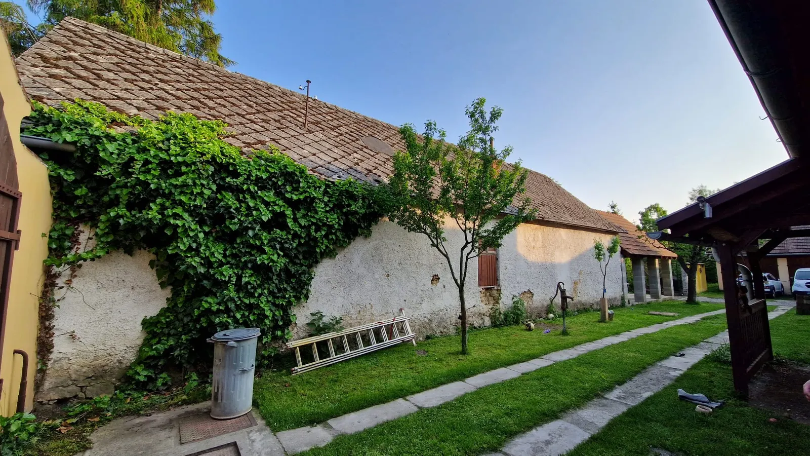 BEFORE renovation (05/2023) — inner courtyard with the outbuilding, original clay roof tiles, ivy-covered wall and an old hand water pump