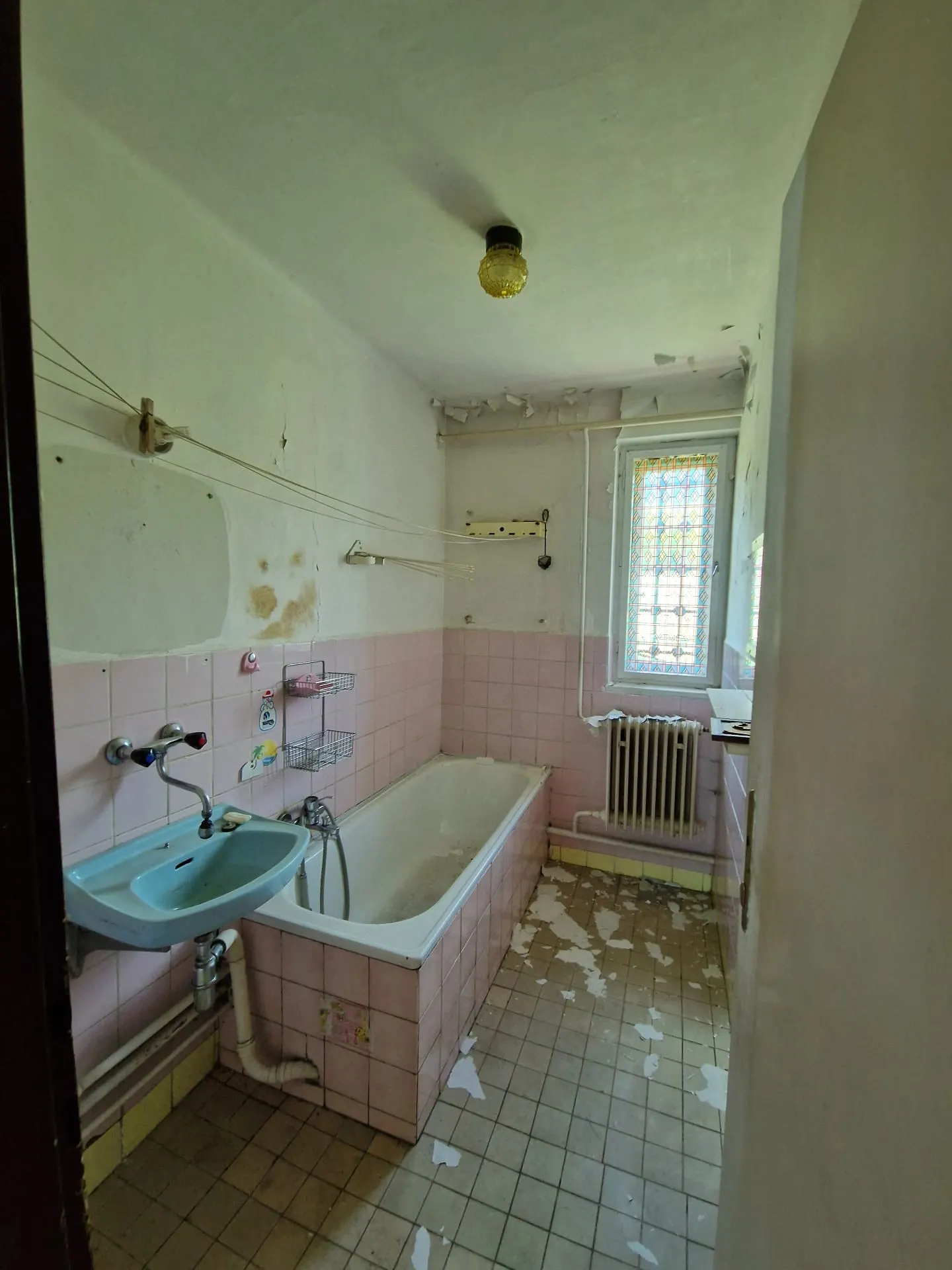 BEFORE renovation (05/2025) — original bathroom with pink tiles, a cast-iron tub, blue washbasin and stained-glass window. The entire sanitary core will be replaced with a new wellness-oriented design.