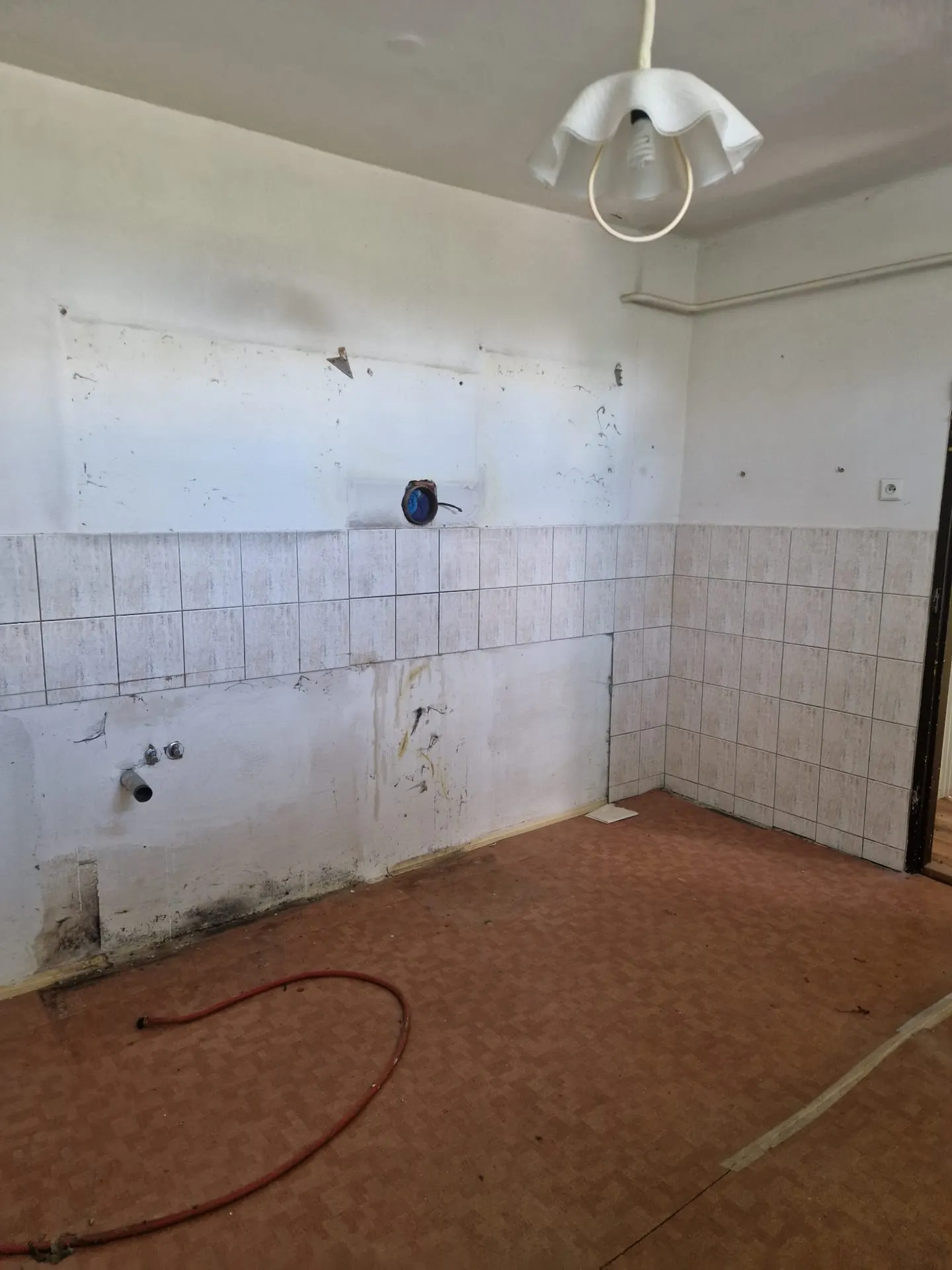 BEFORE renovation (05/2025) — original kitchen after removal of the furniture, with exposed plumbing connections, old tiling and PVC flooring. The space is ready for strip-out and a full refurbishment.