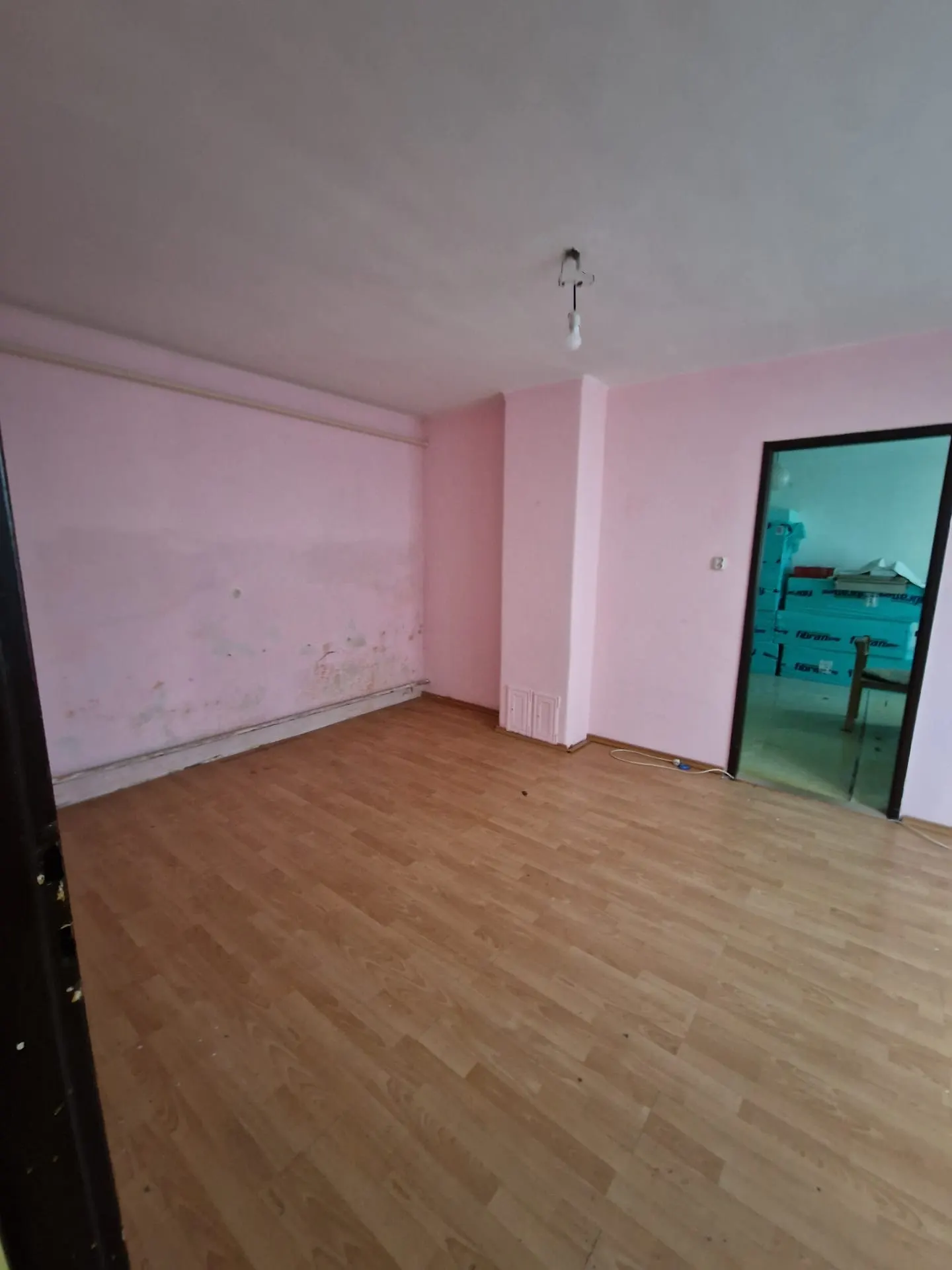 BEFORE renovation (05/2025) — original room with pink walls, laminate flooring and visible damp traces along the skirting. The space awaits remediation, new surfaces and a wellness-oriented layout.